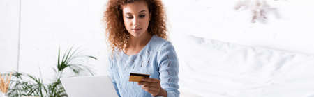 Panoramic crop of red haired woman holding credit card during online shopping at home