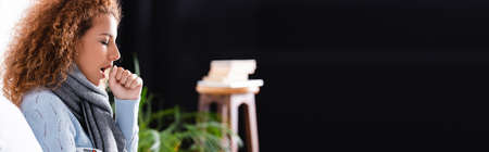 Horizontal crop of young woman with thermometer coughing at homeの写真素材