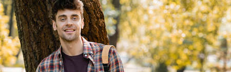 panoramic orientation of man in checkered shirt looking at camera near tree trunk