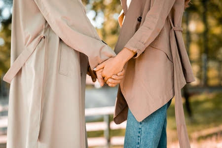 partial view of man and woman in trench coats holding hands in park