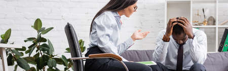horizontal image of psychologist gesturing while talking to upset african american patient holding...