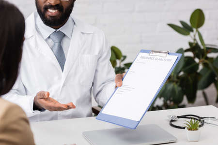 partial view of african american doctor pointing with hand at insurance claim form near patientの写真素材