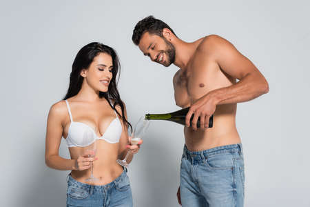 shirtless man pouring champagne in glass near sexy woman in bra on grayの写真素材