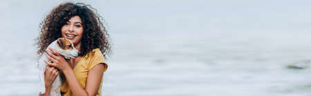 horizontal image of joyful woman hugging jack russell terrier dog near river