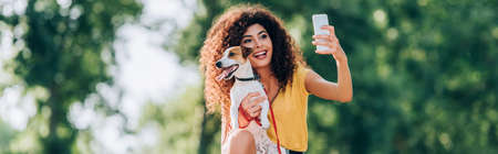 horizontal concept of excited woman taking selfie on mobile phone with jack russell terrier dogの写真素材