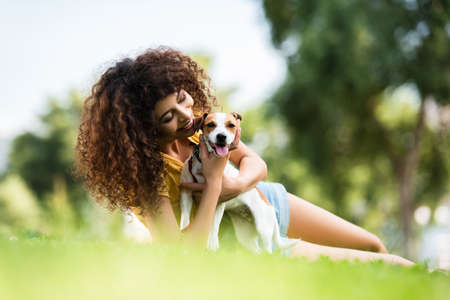selective focus of joyful woman hugging jack russell terrier dog while lying on lawnの写真素材