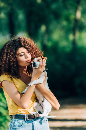 curly woman in summer outfit making duck face while holding jack russell terrier dog in parkの写真素材