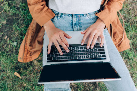 Top view of teleworker in raincoat using laptop with blank screen on grassy lawnの写真素材