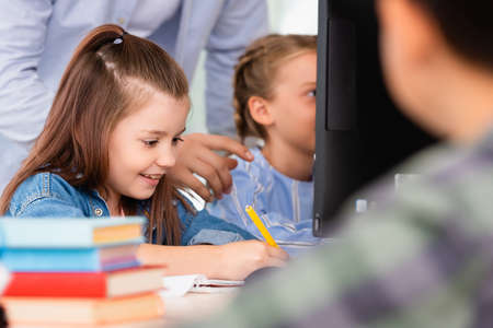 Selective focus of teacher standing near schoolgirl writing on notebook in stem schoolの写真素材