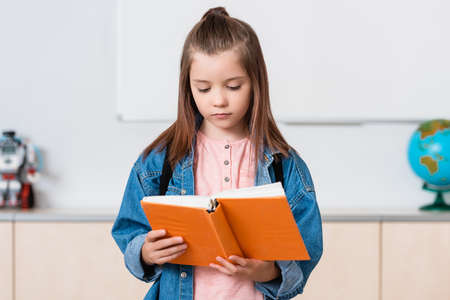 Schoolgirl with backpack reading book in stem school