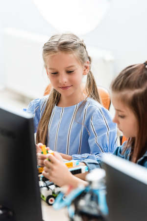 Selective focus of schoolgirls programming robot near computer in school