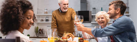 selective focus of african american girl near family clinking glasses of white wine during thanksgiving dinner, horizontal imageの写真素材