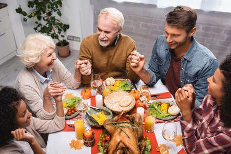 high angle view of multiethnic family holding hands and celebrating thanksgiving at home