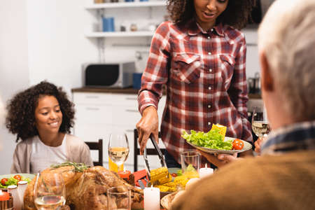 african american woman serving vegetables while celebrating thanksgiving day with multicultural familyの写真素材