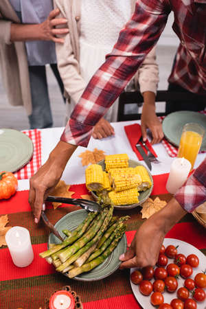Cropped view of african american woman putting asparagus on table during thanksgiving dinner