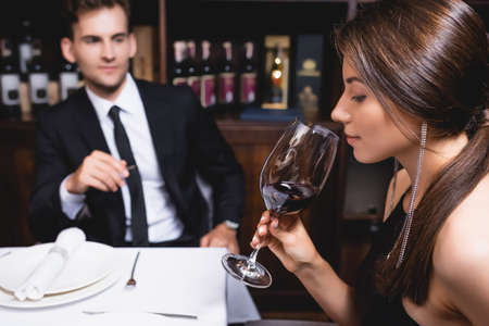 Selective focus of young woman holding glass of wine near boyfriend in restaurant