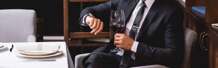 Website header of man in suit holding glass of wine and checking time in restaurantの写真素材