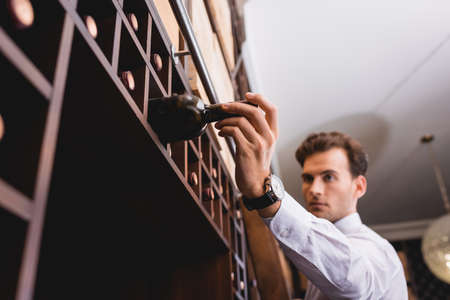 Selective focus of sommelier taking wine bottle from rack in restaurantの写真素材
