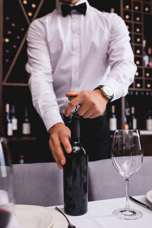 Cropped view of sommelier opening bottle of wine with corkscrew in restaurant