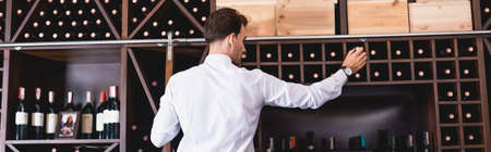 Panoramic shot of sommelier taking wine bottle from rack in restaurantの写真素材