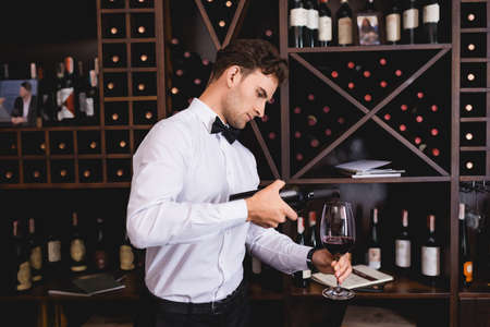 Young sommelier pouring wine in glass in restaurantの写真素材