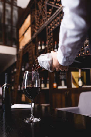 Selective focus of sommelier in shirt pouring wine from decanter in glass