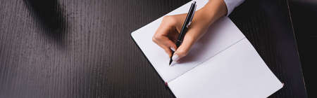 Horizontal image of woman writing on notebook at table