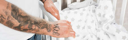 cropped view of tattooed man standing near crib, panoramic conceptの写真素材
