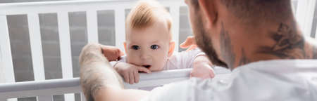 panoramic concept of young father supporting infant son standing in cribの写真素材