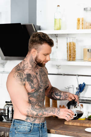 bearded, tattooed man pouring coffee while standing in kitchenの写真素材
