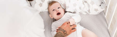 tattooed man touching infant child lying in crib, panoramic concept