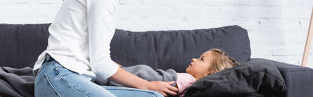 Horizontal crop of woman sitting beside diseased daughter on sofa at home