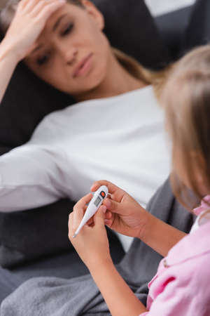 Selective focus of kid holding thermometer beside mother touching foreheadの写真素材