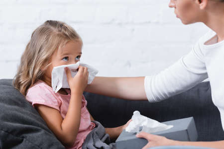 Selective focus of sick child holding napkin during snuffle near mother