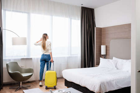 young woman standing with yellow luggage in hotel roomの写真素材