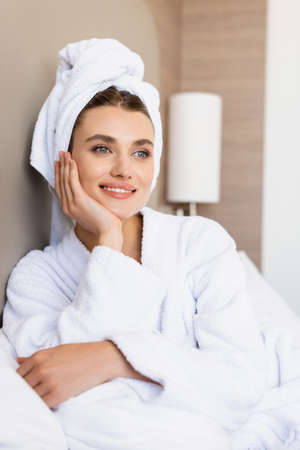 dreamy woman in towel and white bathrobe looking away in hotel roomの写真素材