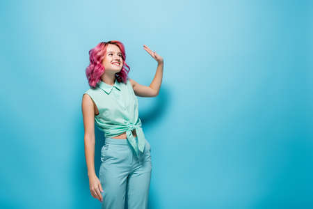 young woman with pink hair waving hand on blue background