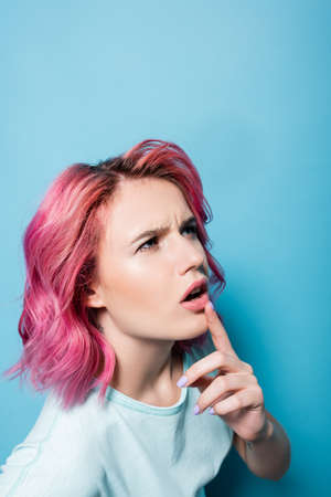 pensive young woman with pink hair on blue background