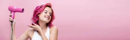 young woman with colorful hair using hairdryer isolated on pink, panoramic shotの写真素材