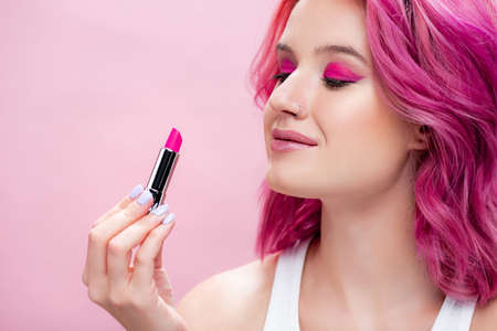 young woman with colorful hair holding lipstick isolated on pinkの写真素材
