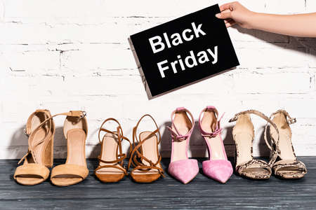 cropped view of woman holding placard with black friday lettering near shoes and brick wall