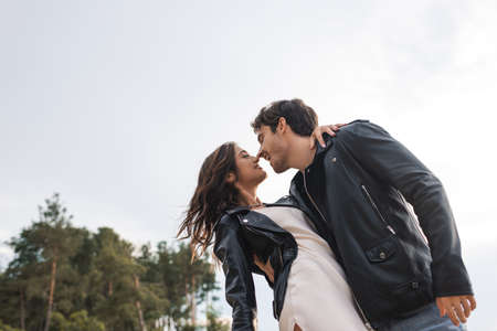 Low angle view of man in leather jacket kissing girlfriend in dress outdoorsの写真素材