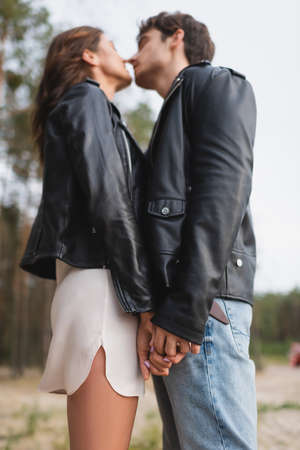 Low angle view of young couple in leather jackets holding hands and kissing in forest