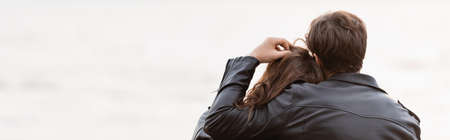 Horizontal crop of man touching hair of girlfriend in leather jacket near sea