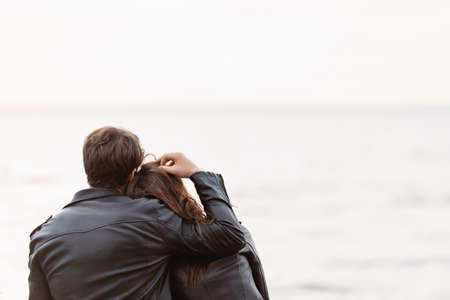 Back view of man in leather jacket touching hair of girlfriend near sea