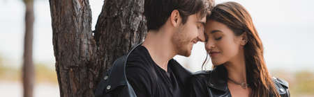 Website header of man in leather jacket standing near girlfriend and tree in forest