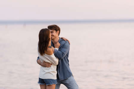 Young man kissing girlfriend near sea at evening