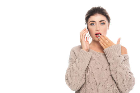 shocked woman in stylish openwork sweater covering mouth with hand while talking on smartphone...