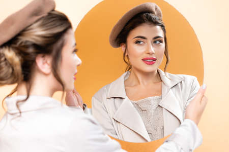 selective focus of trendy woman in autumn outfit looking in mirror on peach