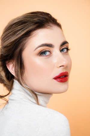 portrait of sensual woman with red lips looking at camera isolated on peach